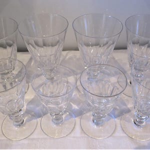 May include: Eight clear, stemmed drinking glasses. Four are taller with a flared bowl and four are shorter with a rounded bowl. All have a decorative etched pattern and sit on a round base.
