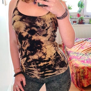May include: A black and tan tie-dye tank top with a scoop neck and thin straps. The tank top is paired with dark denim shorts.