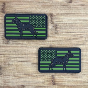 May include: Two black and green patches with a silhouette of a German Shepherd dog in front of an American flag. The flag has green stripes and white stars on a black background.