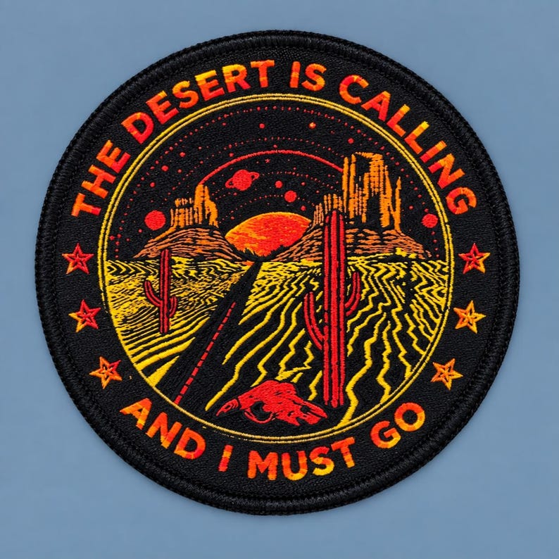 Round black desert patch with orange “The Desert Is Calling and I Must Go” lettering, featuring a sunset, cacti, desert road, stars, and skull design on a blue-gray background.