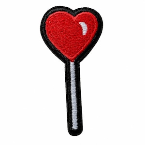 May include: An embroidered patch in the shape of a heart-topped lollipop. The heart is bright red with a small white highlight, outlined in black thread. The stick is white with a black border, creating a clean, graphic design for this accessory.