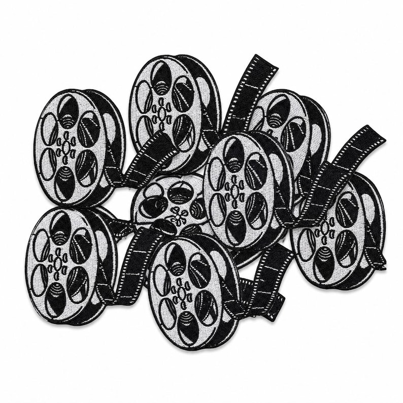 Loose pile of black and white embroidered film reel patches layered together on a square white background.