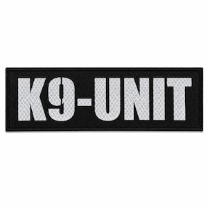 May include: A rectangular black patch with a stitched border. The text K9-UNIT is displayed in large, bold, reflective silver lettering with a visible honeycomb pattern across the surface of the letters, set against the solid black background.