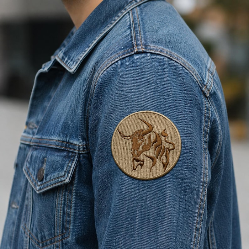 Round tan Taurus zodiac patch with a brown bull logo sewn onto the shoulder sleeve of a blue denim jacket.