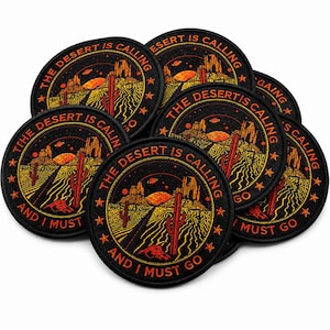 Loose pile of round black embroidered “The Desert Is Calling And I Must Go” patches with orange, red, and yellow desert scene artwork, overlapping on a clean white background.