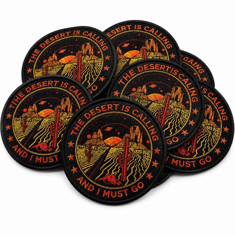 Loose pile of round black embroidered “The Desert Is Calling And I Must Go” patches with orange, red, and yellow desert scene artwork, overlapping on a clean white background.