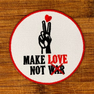 May include: White embroidered patch with a red border. The patch features a peace sign, a red heart, and the text "Make Love Not War" with the word "War" crossed out.