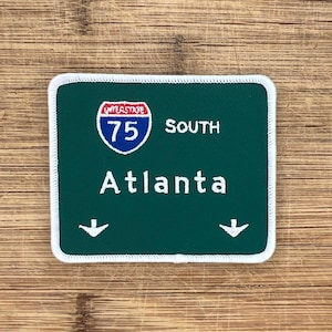 May include: Green and white interstate highway sign with white text that reads "Interstate 75 South Atlanta" with two white downward arrows.