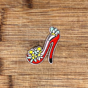 May include: Red high heel shoe with a floral design on the toe. The shoe is made of fabric and has a white and yellow flower pattern.
