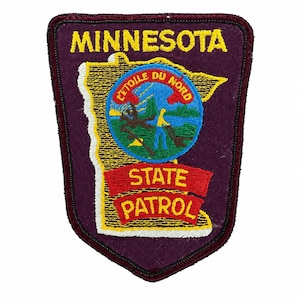 Könnte beinhalten: Ein schildförmiger, bestickter Aufnäher mit dunkelviolettem Hintergrund. Er zeigt den gelben Schriftzug MINNESOTA über einer gelb umrandeten Karte des Bundesstaates. In der Karte befindet sich ein kreisförmiges Emblem mit dem Text L'ETOILE DU NORD und STATE PATROL.
