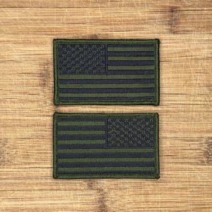 Może przedstawiać: Dwa zielono-czarne naszywki z flagą Stanów Zjednoczonych. Naszywki znajdują się na drewnianej powierzchni.