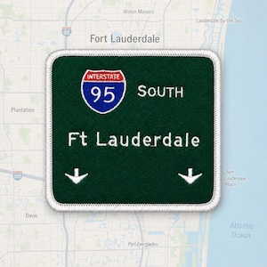 May include: A square embroidered patch with a dark green background and a white border. It features the Interstate 95 shield logo in red, white, and blue, the text SOUTH, the text Ft Lauderdale, and two white downward-pointing arrows.