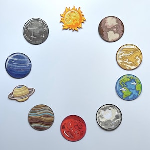 May include: A collection of embroidered patches depicting planets and the sun. The patches are circular, with detailed designs and vibrant colors. The sun patch is yellow and orange, while the planets feature shades of blue, brown, red, and gray.