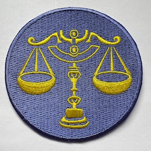 May include: A blue embroidered patch with a yellow scale design. The scales are balanced on a stand with a decorative top.