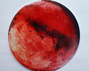 May include: A round, red and black illustration of the planet Mars. The image features a detailed depiction of the planet's surface, with craters and dark patches. The artwork is set against a white background.