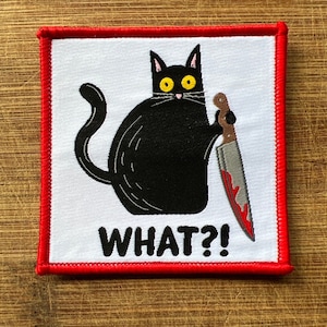 May include: A black cat with yellow eyes holds a bloody knife and says "WHAT?!" in white text on a white background. The image is surrounded by a red border.