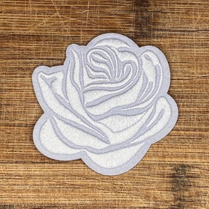 May include: White embroidered rose patch. The rose is a classic floral design with a detailed, layered look.