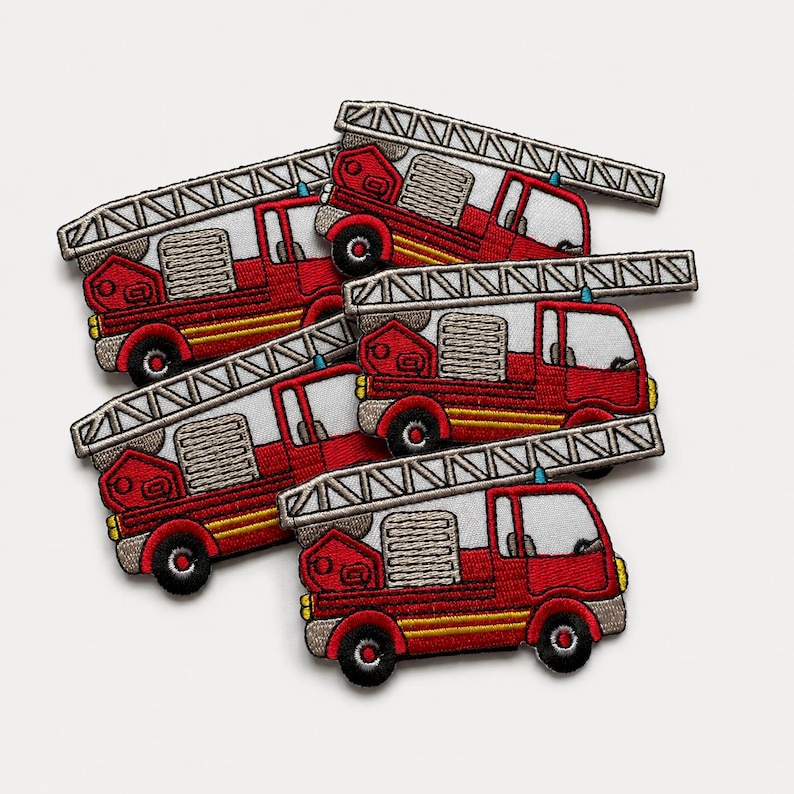 Loose pile of red embroidered fire truck patches with silver ladders, yellow accents, black wheels, and detailed stitched texture on a clean white background.