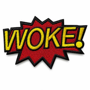 May include: An embroidered patch featuring the word WOKE! in bold yellow capital letters with a black outline. The text is set against a jagged, red, comic-book-style speech bubble shape with a thick black border, creating a vibrant graphic design.