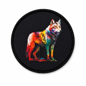 May include: A circular embroidered patch featuring a standing wolf depicted in vibrant, multi-colored abstract paint strokes. The wolf is rendered in shades of red, orange, yellow, blue, and purple against a solid black background with a black border.