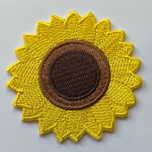 May include: A yellow embroidered sunflower patch with a brown center. The sunflower has a detailed design with multiple layers of petals.