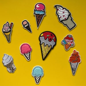 May include: Assortment of colorful embroidered iron-on patches featuring various ice cream cone designs. The patches include a pink ice cream cone with a blue swirl, a blue ice cream cone with a white swirl, a red and white ice cream cone with a chocolate swirl, a pink ice cream cone with a white swirl, a brown ice cream cone with a red swirl, a white ice cream cone with a blue swirl, a yellow ice cream cone with a red swirl, and a white ice cream cone with a red swirl. The patches are perfect for adding a fun and whimsical touch to clothing, bags, and other accessories.