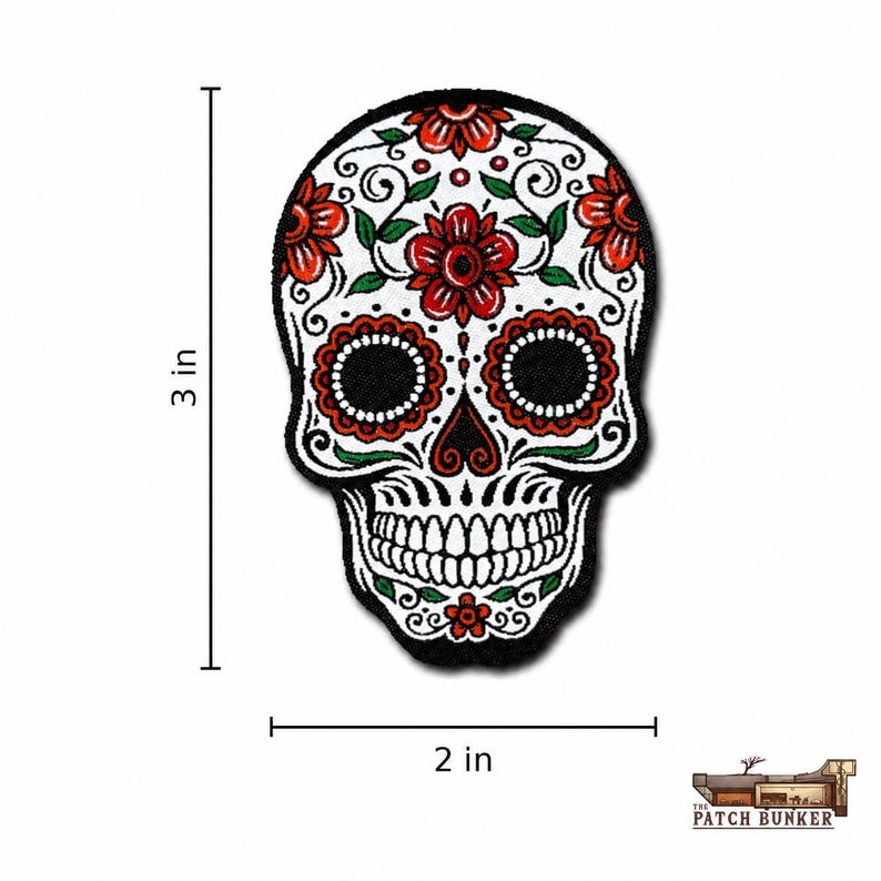 Sugar skull embroidered patch with a white skull face, black border, red-orange flowers, green leaves, black scrollwork, round black eye sockets, and tooth detailing, shown on a clean white square background with 3 in height and 2 in width measurement lines plus The Patch Bunker logo in the lower-right corner.