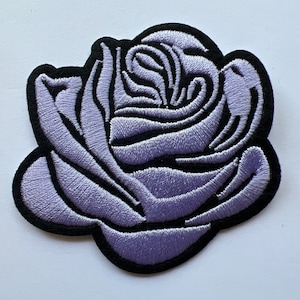 May include: A lavender embroidered rose patch with black outline. The rose is a single bloom with a curled center.