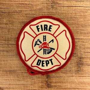 May include: Round, embroidered patch with a red border and a cream-colored center. The patch features a red Maltese cross design with the words "FIRE DEPT" in black. Inside the cross are firefighter tools and a helmet.