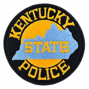 Può includere: Una toppa ricamata circolare con bordo nero. Il centro presenta un cerchio giallo dietro una mappa azzurra del Kentucky. Il testo KENTUCKY STATE POLICE è ricamato in giallo, con KENTUCKY arcuato in alto e POLICE nella parte inferiore.