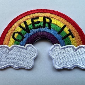 May include: Embroidered rainbow patch with white clouds and the text "Over It" in black.