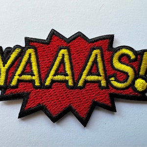 May include: A red and yellow embroidered patch with the word "YAAAS!" in a comic book style font.