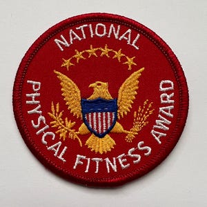May include: A circular, red embroidered patch with the words "NATIONAL PHYSICAL FITNESS AWARD" in white. It features a gold eagle with a blue and white shield, and a ring of gold stars.
