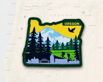 May include: A shaped embroidered patch in the outline of the state of Oregon. The design features a yellow sky, a light blue mountain, dark green pine trees, and a light green meadow. Two hikers and a bird are visible with the text OREGON.