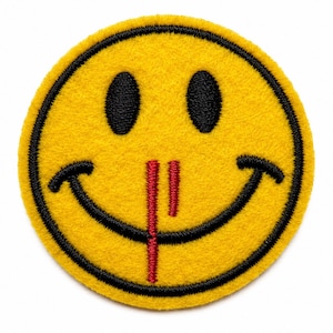 May include: A circular embroidered patch featuring a bright yellow smiley face with black stitched eyes and a wide black curved mouth. A vertical red stitched line extends downward from the nose area, crossing over the center of the mouth.