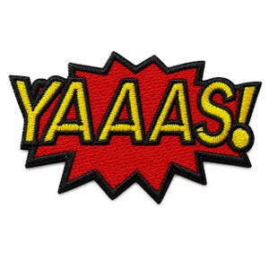 May include: An embroidered patch featuring the word YAAS! in bold yellow letters with a thick black outline. The text is set against a jagged, comic book-style speech bubble shape filled with a vibrant red color and a black border outline.