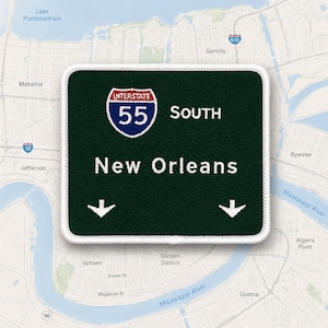 May include: A rectangular embroidered patch with a dark green background and a white border. It features the Interstate 55 shield logo, the text SOUTH, the text New Orleans, and two white downward-pointing arrows, all in white embroidery.