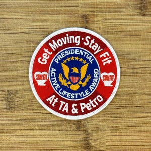 May include: A circular embroidered patch with the text "Get Moving Stay Fit" in white on a red background. The center features a blue circle with a gold eagle and the words "Presidential Active Lifestyle Award." Two small white hearts with "Stay Fit" are on the sides.