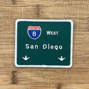Può includere: Segnale stradale verde e bianco con il testo Interstate 8 West San Diego e una freccia bianca che punta verso il basso su entrambi i lati.