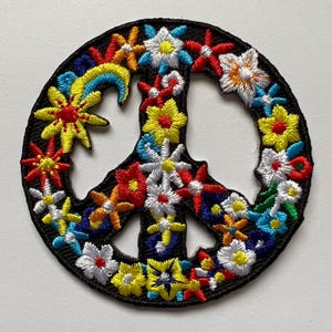 May include: A colorful peace sign patch with a black background and embroidered flowers in shades of red, yellow, blue, white, and orange.
