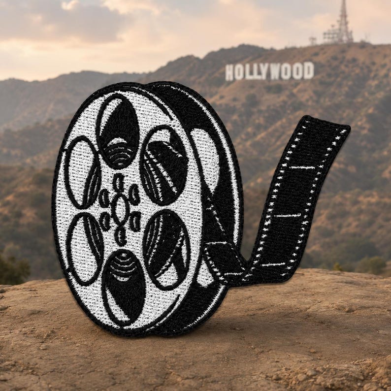 Black and white embroidered film reel patch with curling filmstrip detail and iron-on backing.