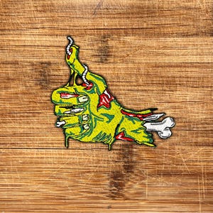 May include: A green and red zombie hand giving a thumbs up with a bone sticking out of the wrist. The hand is dripping with green goo.