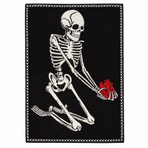 May include: A rectangular embroidered patch featuring a white skeleton kneeling on a black background. The skeleton holds a bright red anatomical heart in its hands. The entire design is framed by a white stitched border with an X-pattern.