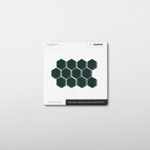 May include: A sample card featuring dark green, hexagonal tiles arranged in a honeycomb pattern. The card has the word "SAMPLE" printed on it, along with the brand name "CEMENTO". The text "Slight variance in shade may occur between production batches" is also visible.