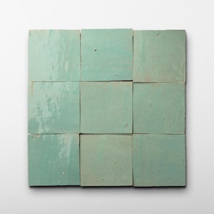 May include: Nine square, seafoam green tiles arranged in a grid. The tiles have a slightly uneven surface and a matte finish. The color varies slightly across the tiles, creating a subtle visual texture. The tiles are likely for use in a kitchen or bathroom.