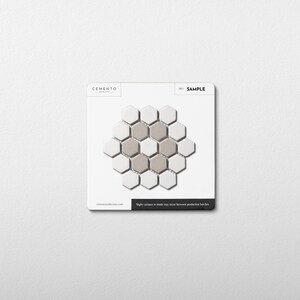 May include: A sample tile card featuring a honeycomb pattern. The pattern is composed of white and gray hexagonal tiles. The card has the word "SAMPLE" printed on it, along with the brand name "CEMENTO". The bottom of the card has the website address and a disclaimer.