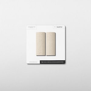 May include: Two rectangular samples of Cemento, a light beige material, are displayed on a white card. The word "SAMPLE" is printed on the card. The bottom of the card has the text "Slight variance in shade may occur between production batches."