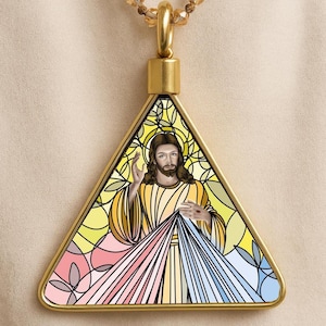 May include: Gold-toned pendant with a triangular stained-glass design. The pendant features an image of Jesus with outstretched hand, surrounded by yellow, pink, and blue rays. The pendant hangs from a gold chain.