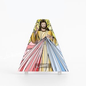 Puede incluir: Una pieza de arte triangular de vidrieras que representa a Jesucristo con las manos extendidas. La obra de arte presenta colores vibrantes, incluyendo amarillo, rosa y azul, que irradian desde el centro. La pieza está montada sobre pies transparentes y redondeados.