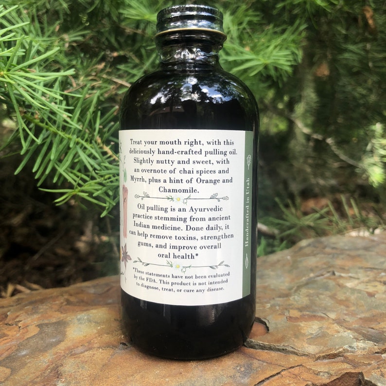 May include: A dark glass bottle containing pulling oil with a white rectangular label. The label text reads: Treat your mouth right, with this deliciously hand-crafted pulling oil. Slightly nutty and sweet, with an overnote of chai spices and Myrrh, plus a hint of Orange and Chamomile. Oil pulling is an Ayurvedic practice stemming from ancient Indian medicine. Done daily, it can help remove toxins, strengthen gums, and improve overall oral health. Handcrafted in Utah.